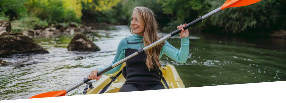 A woman smiling while kayaking in a river.