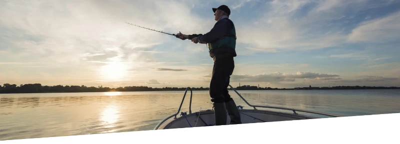 A man happily fishing on a boat in the middle of a lake at sunrise.