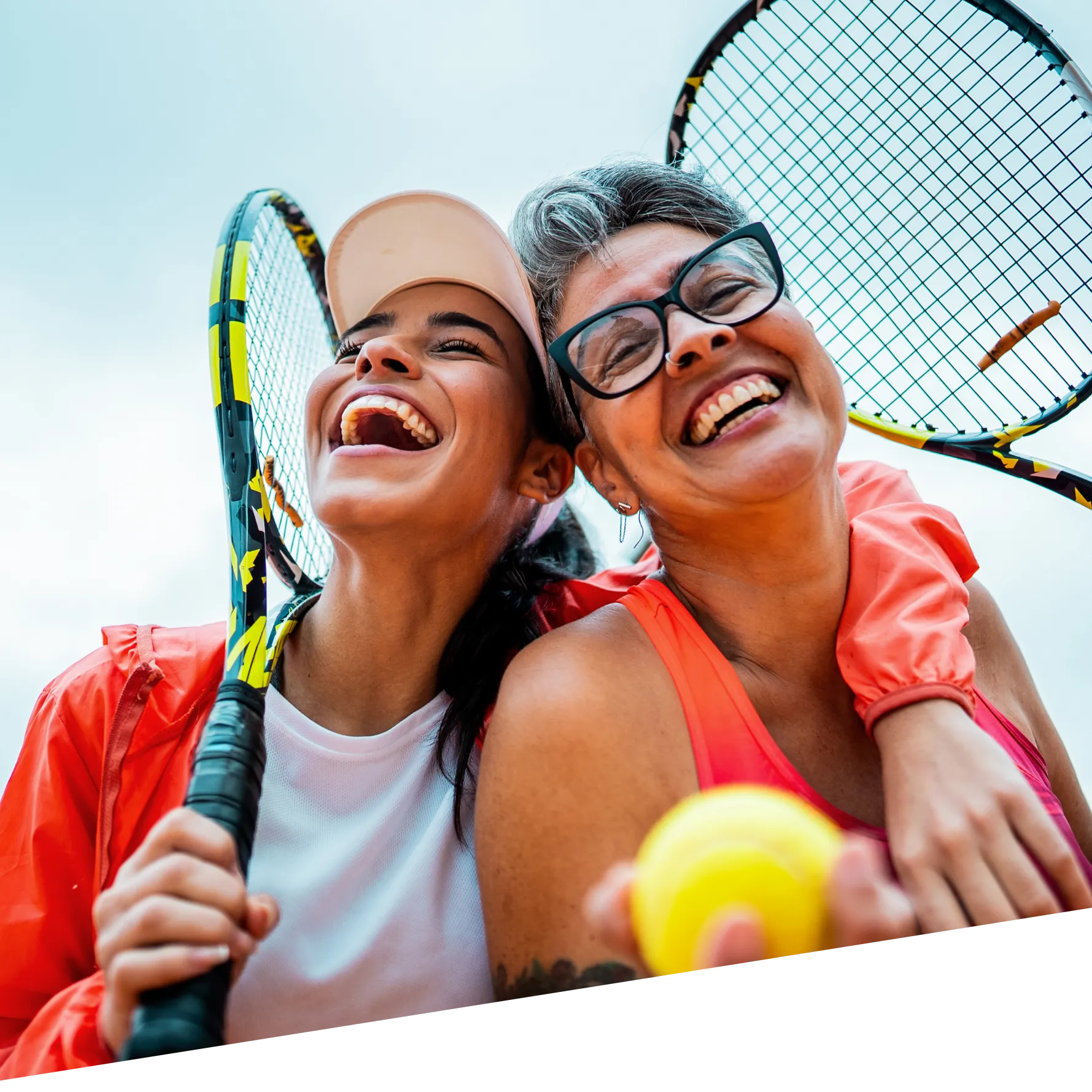 An image of two women happily outside with tennis equipment.
