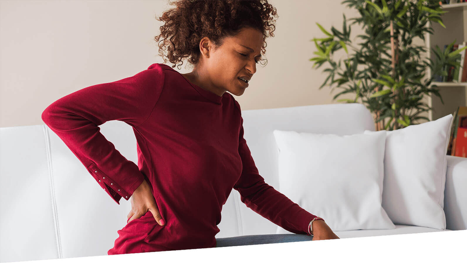 A woman holds her back, and winces in pain.