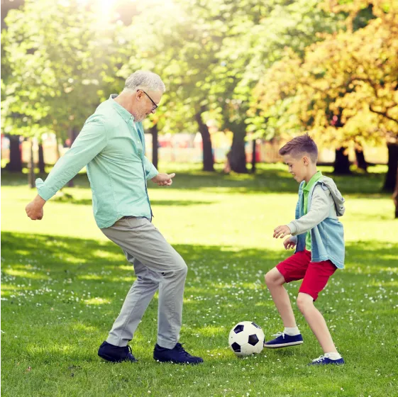 Happy grandfather and grandson playing football at summer park