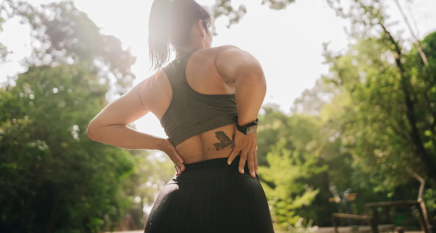 A young woman standing outside suffering from a back pain cramp.
