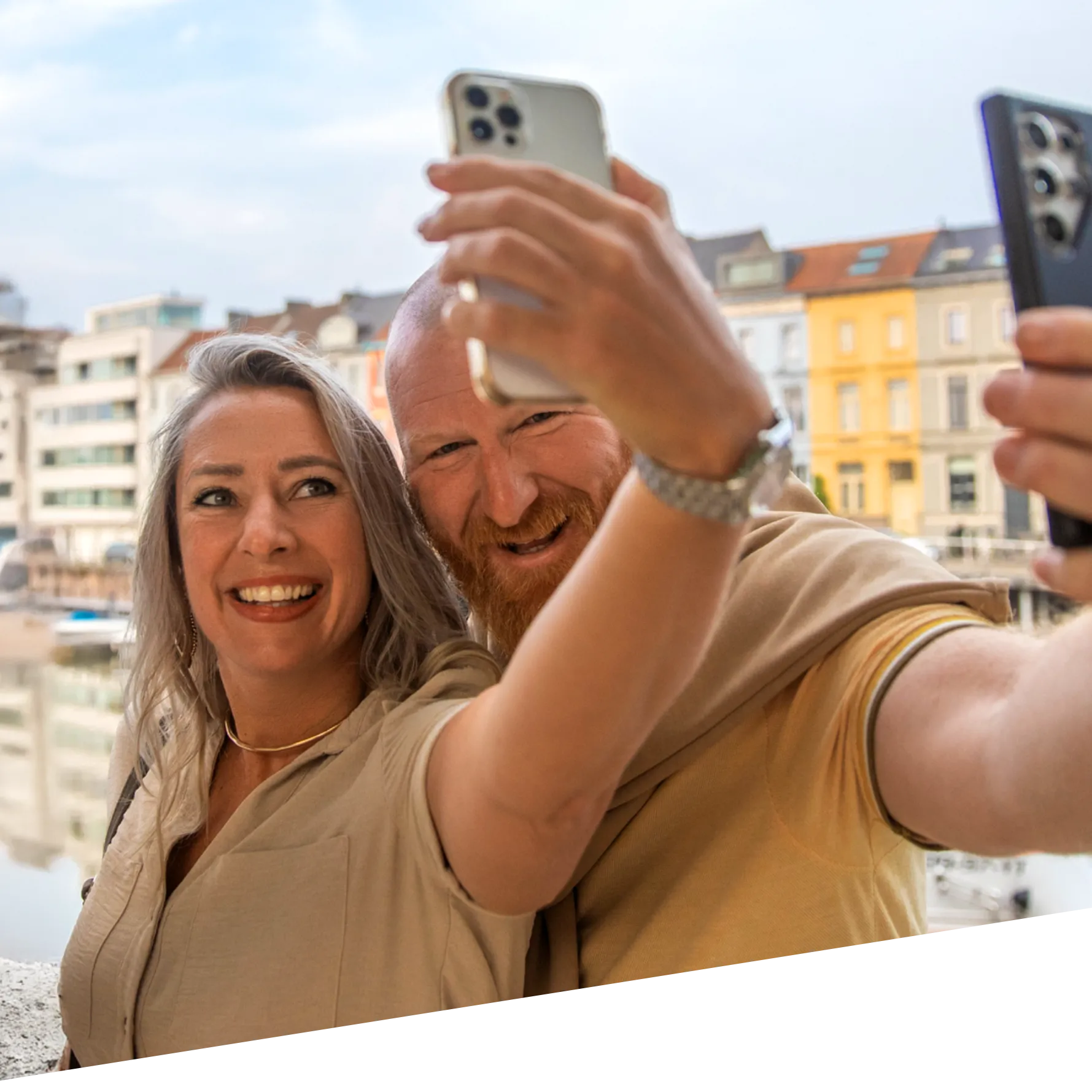 A man and a woman smiling while taking photos with their phones.